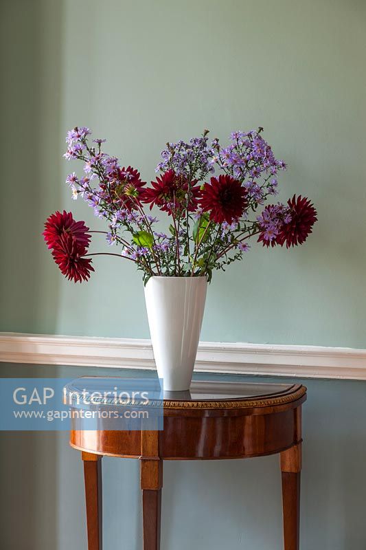 Red and purple flowers in white vase on antique console table 