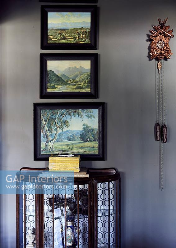 Glass display case and framed paintings on grey wall 