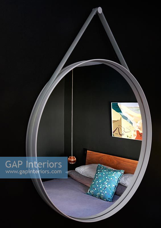 Contemporary bedroom seen through suspended circular mirror 