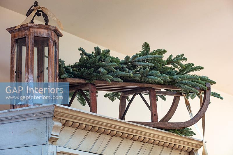 Sprigs of fir on wooden sledge on top of wardrobe with lantern 