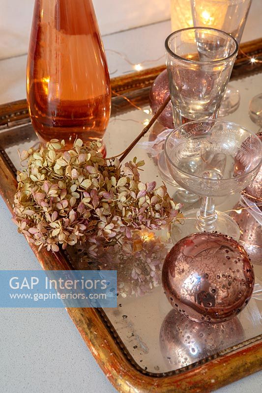 Bronze and gold decorations on tray with glasses and dried hydrangea flower