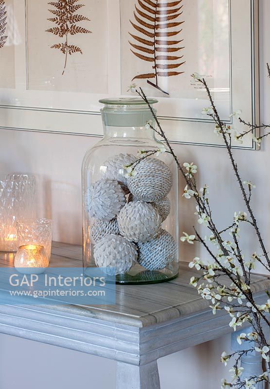 Decorative woven baubles in glass jar on white table 