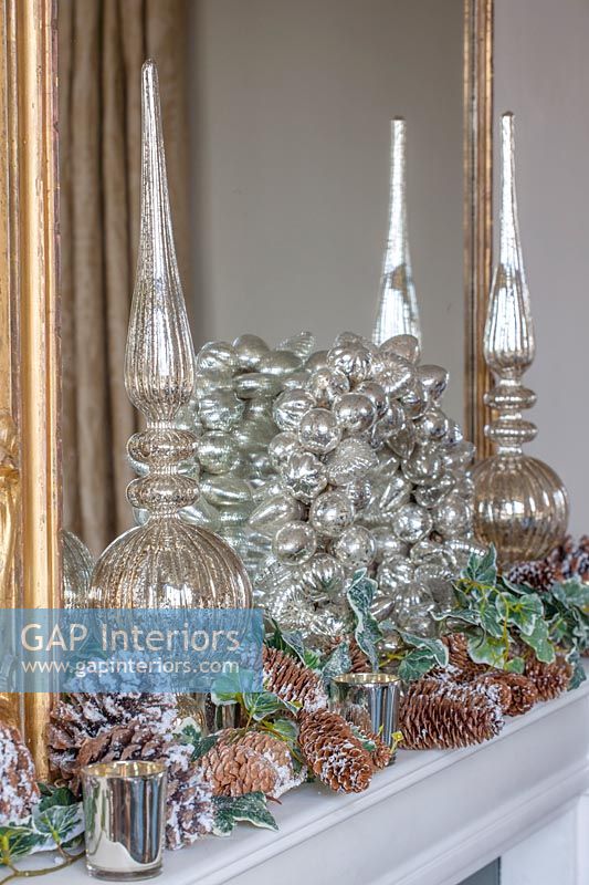 Silver glass wreath and garland of pine cones on mantelpiece 