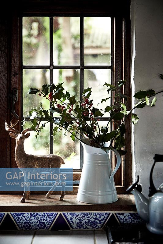 Reindeer ornament and jug of holly on country kitchen windowsill 