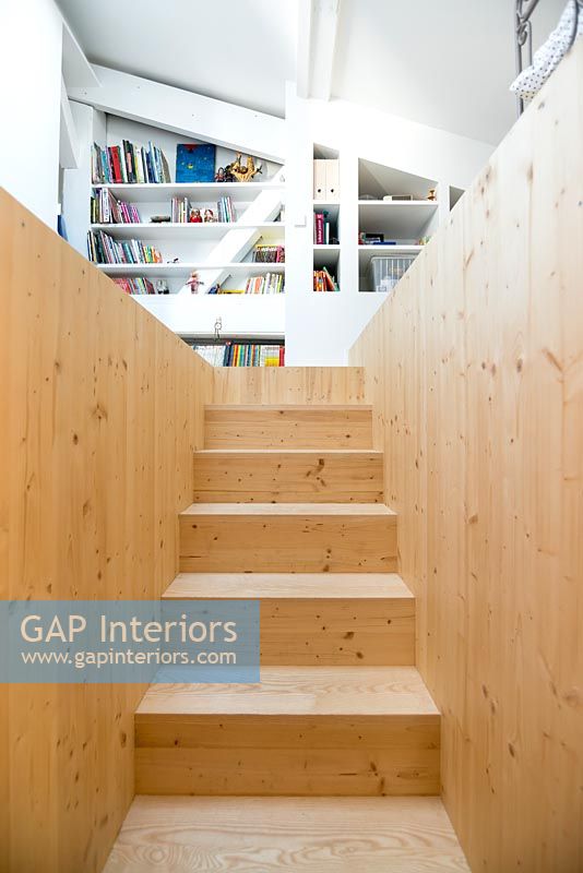 Wooden staircase with view to built-in bookshelves in room upstairs 