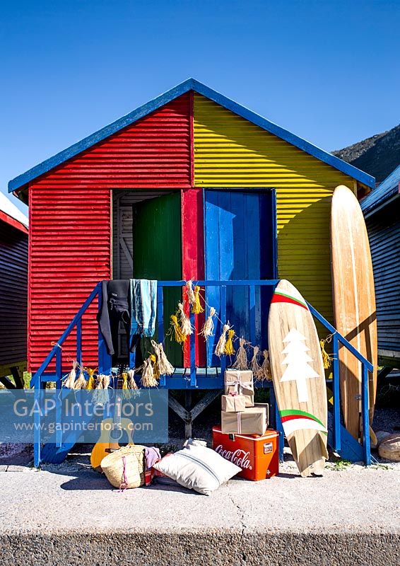 Surfboard and gifts outside colourful beach huts 