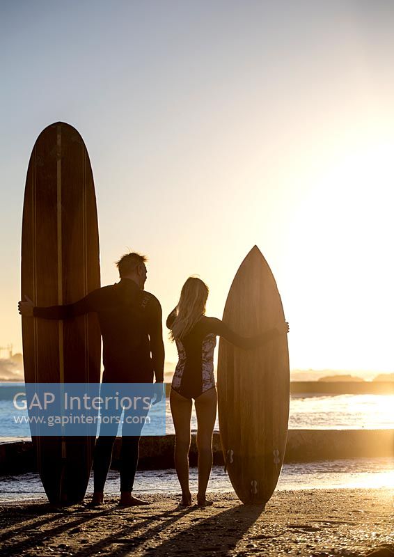 Man and woman standing on beach at sunset holding surfboards