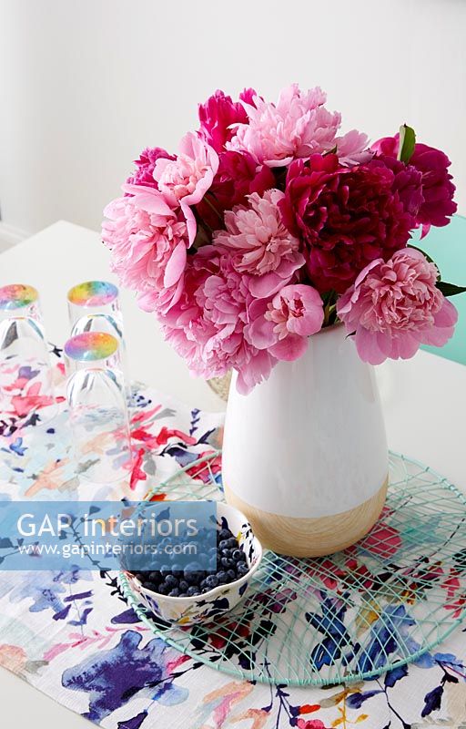 Pink and red flowers in ceramic vase on colourful table 