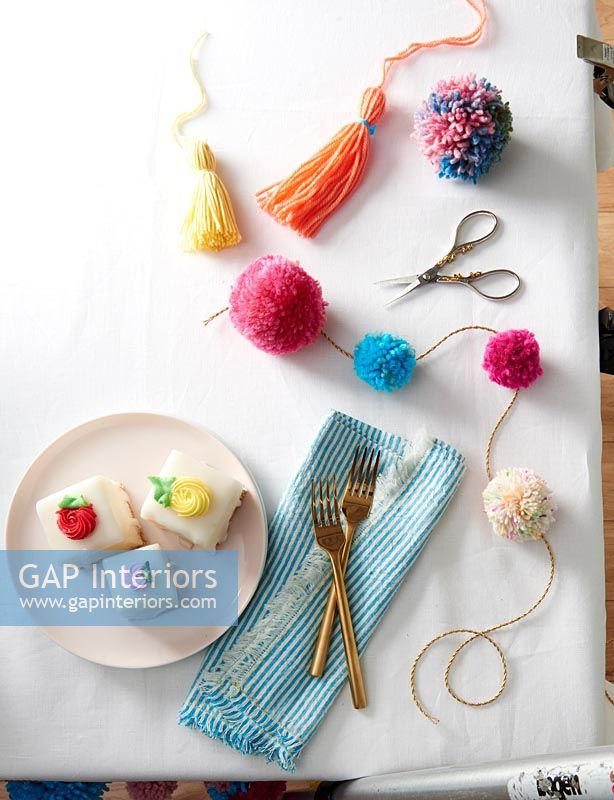 Pom poms and tassels on dining room table with cakes on plate 