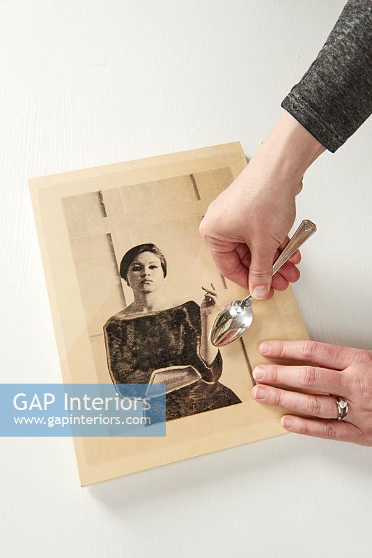 Woman pressing picture to wooden frame using a spoon 