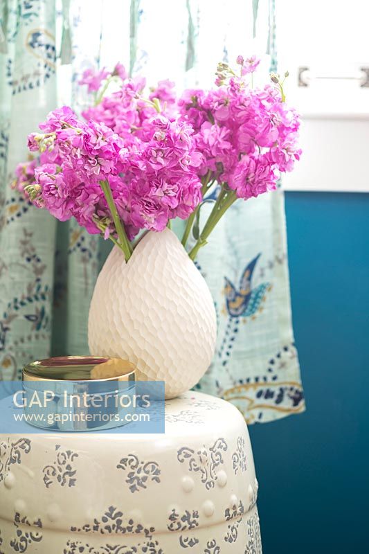 Pink flowers in cream coloured vase on bedside table 