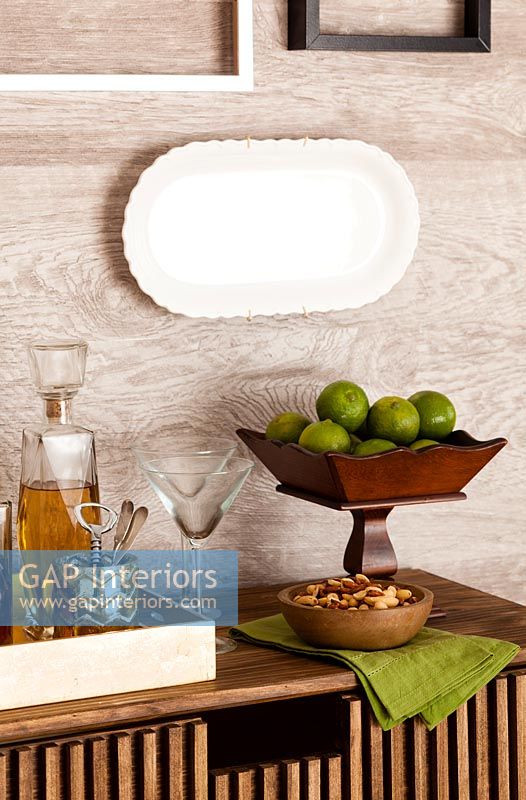 Wooden fruit bowl and cocktail glasses on wooden chest of drawers 