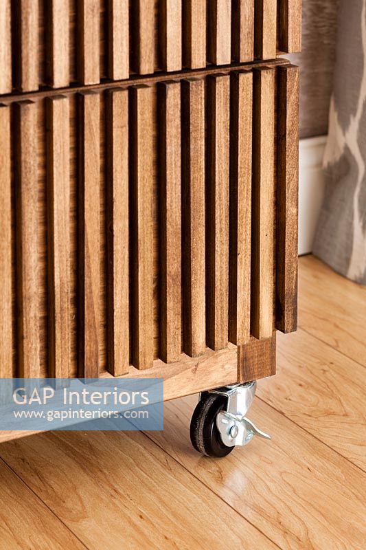 Detail of wooden slatted chest of drawers on castors 