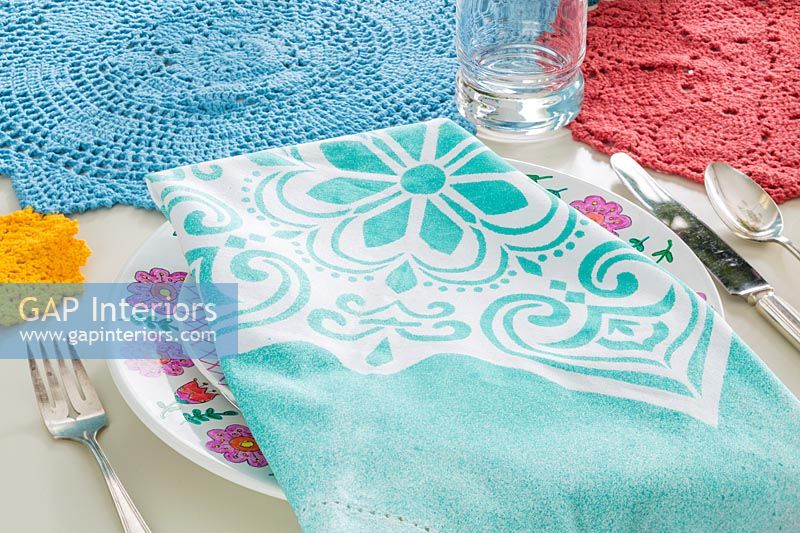 Turquoise patterned napkin and crocheted mats on dining table 