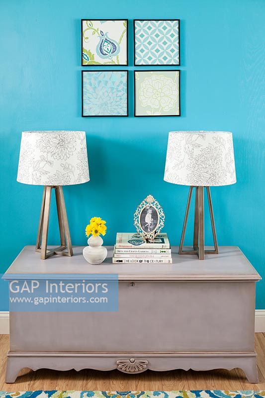 Blanket box with modern lamps next to blue painted wall 