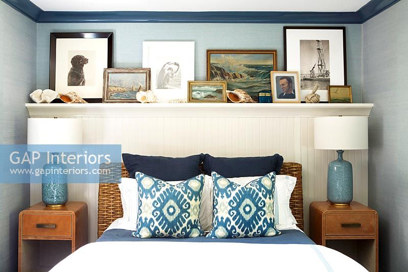 Wooden shelf of framed pictures above bed with rattan headboard 