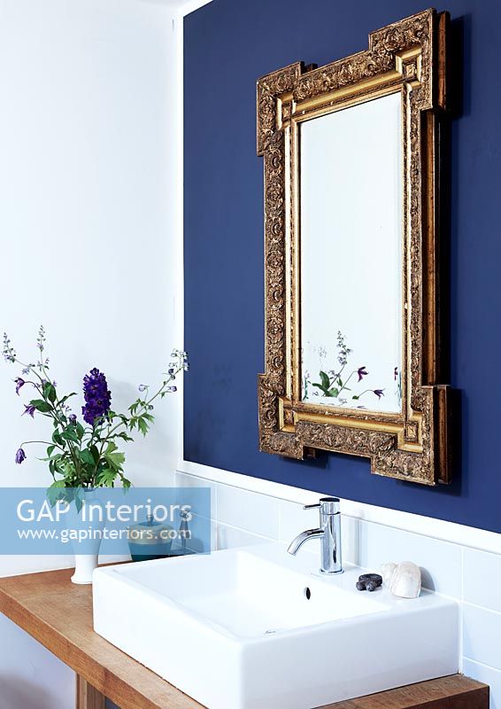 Gold mirror on dark blue wall above bathroom sink 