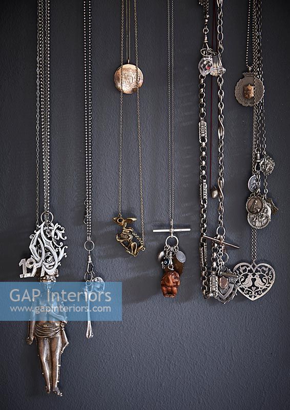 Collection of necklaces hanging on grey painted wall 