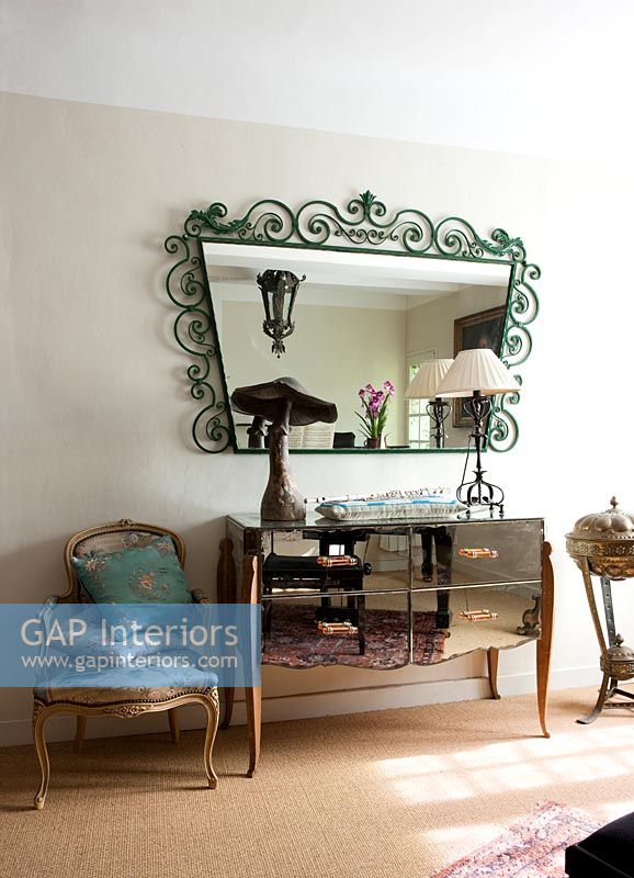 Ornate antique green metal mirror above mirrored sideboard 