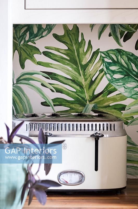 Retro style toaster in front of tropical leaf patterned wallpaper 