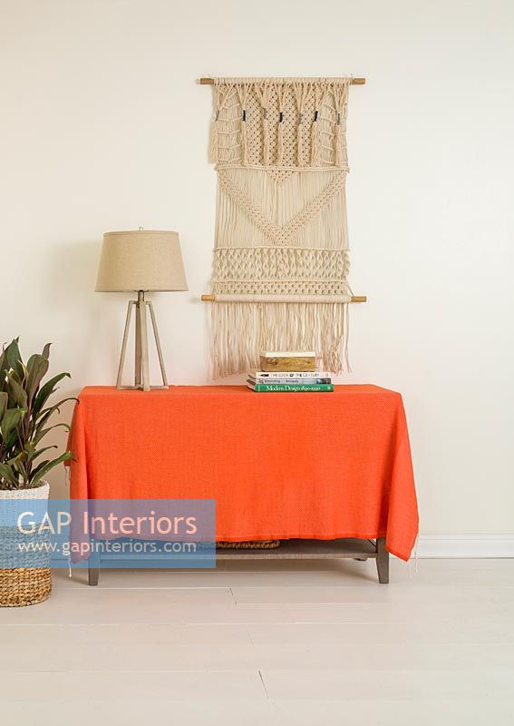 Orange blanket over sideboard with macrame wall hanging 