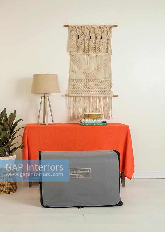 Orange blanket over sideboard with macrame wall hanging and folded bed