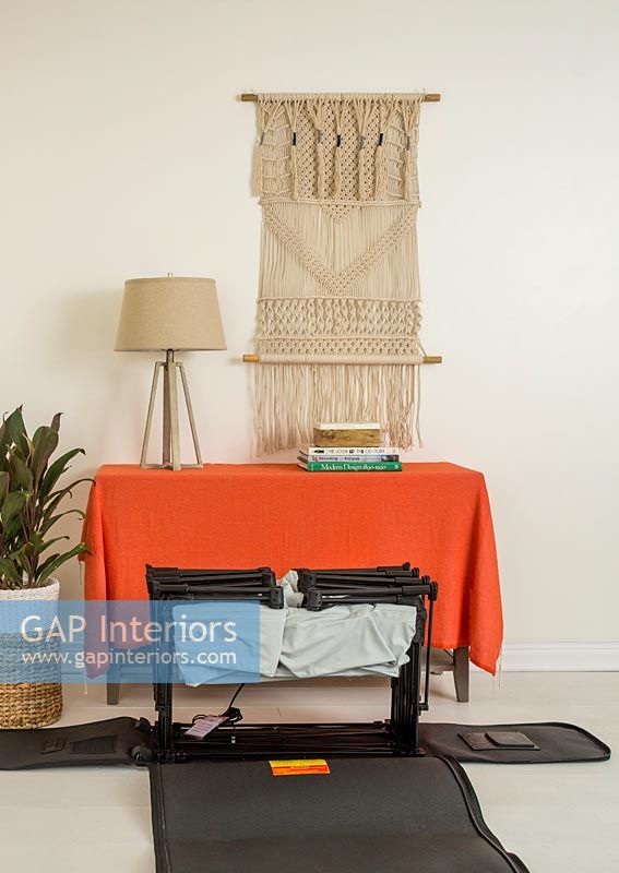 Orange blanket over sideboard with macrame wall hanging and folded bed