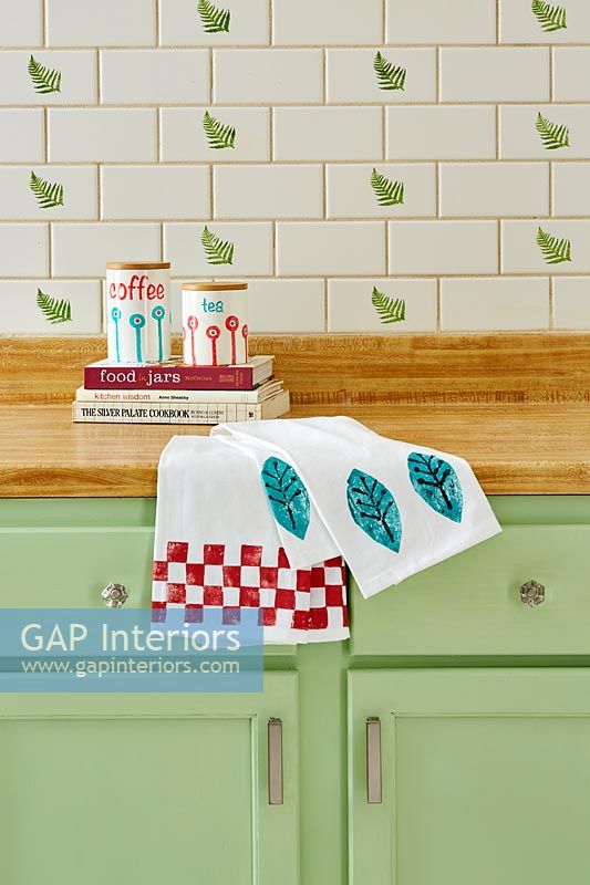 Green kitchen with leaf design on wall tiles and tea towels 