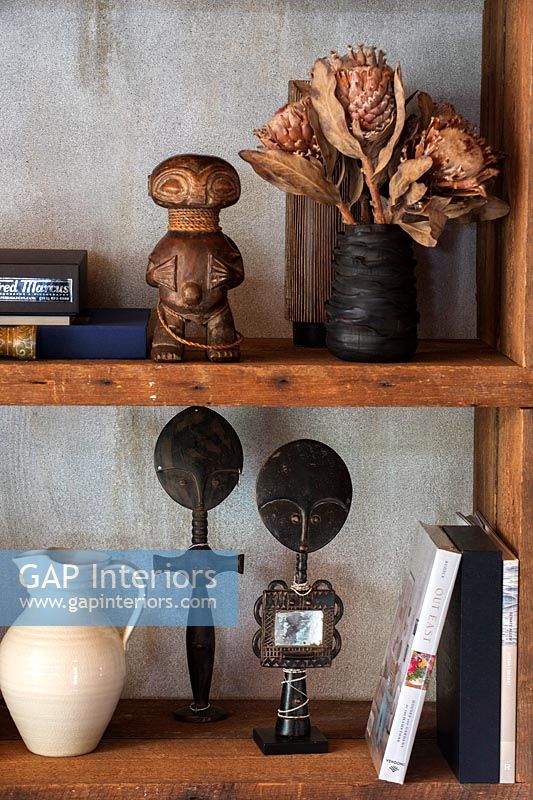 Wooden bookshelves with African ornaments and dried flowers 
