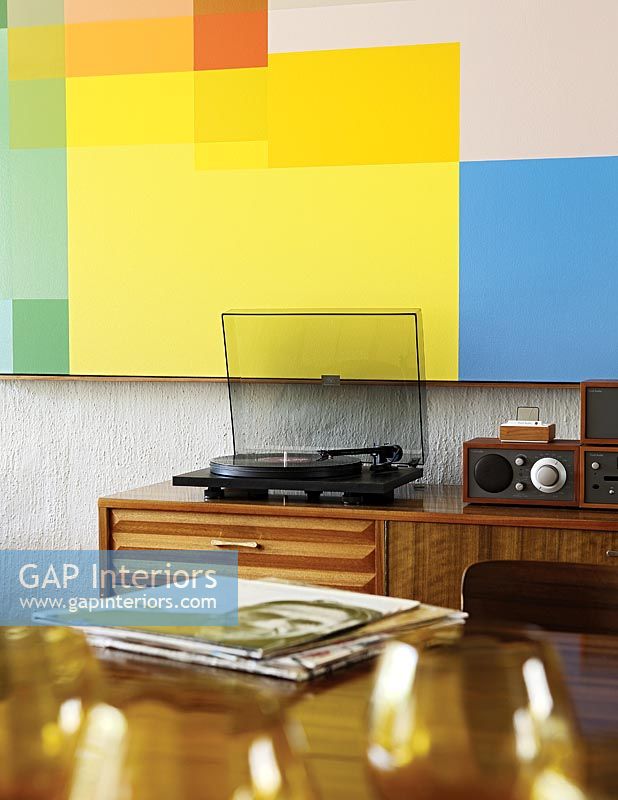 Turntable on sideboard with colourful artwork on wall behind 