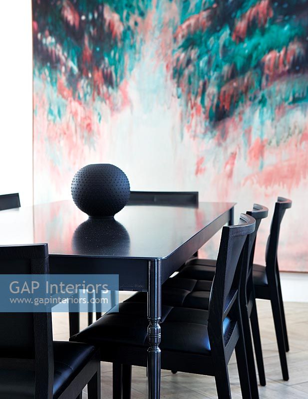 Black dining table and chairs with backdrop of modern artwork 