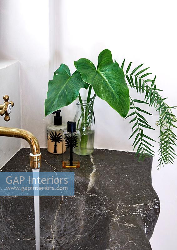 Vase of foliage next to marble sink with running water 