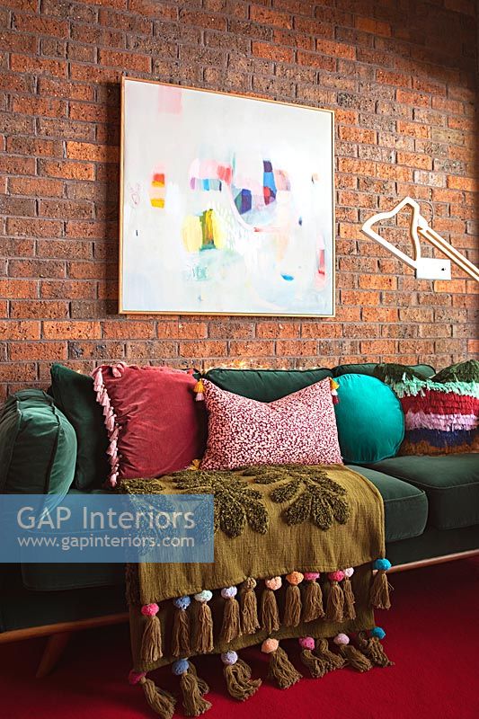 Large green sofa against exposed brickwork wall with framed painting 