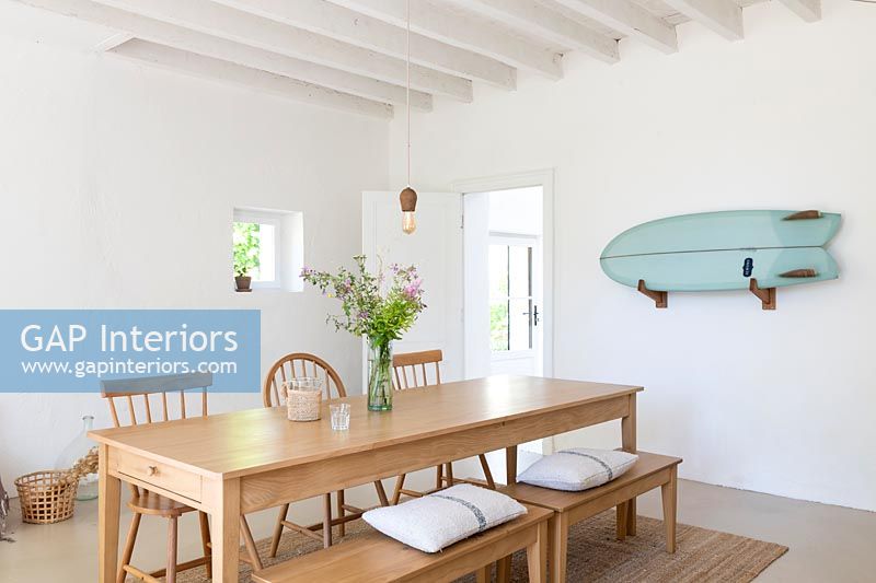 Wall mounted surfboard in white country dining room with wooden furniture 