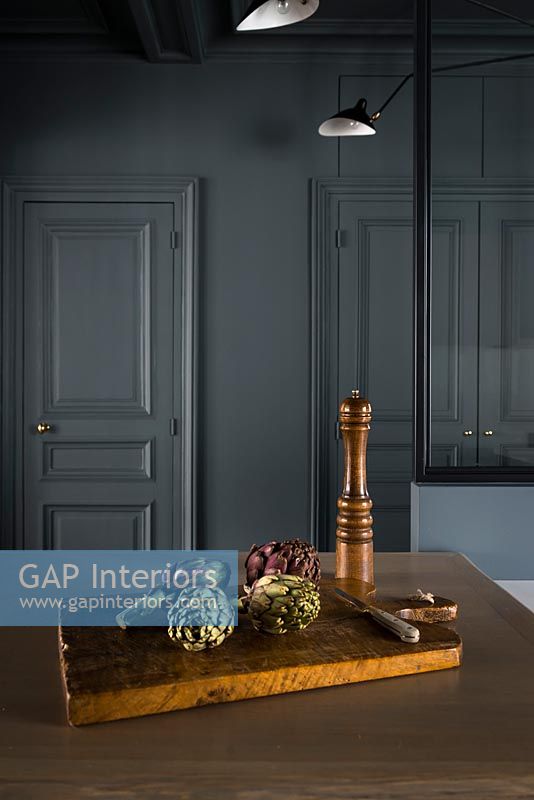 Artichokes on chopping board in kitchen with dark grey painted walls 