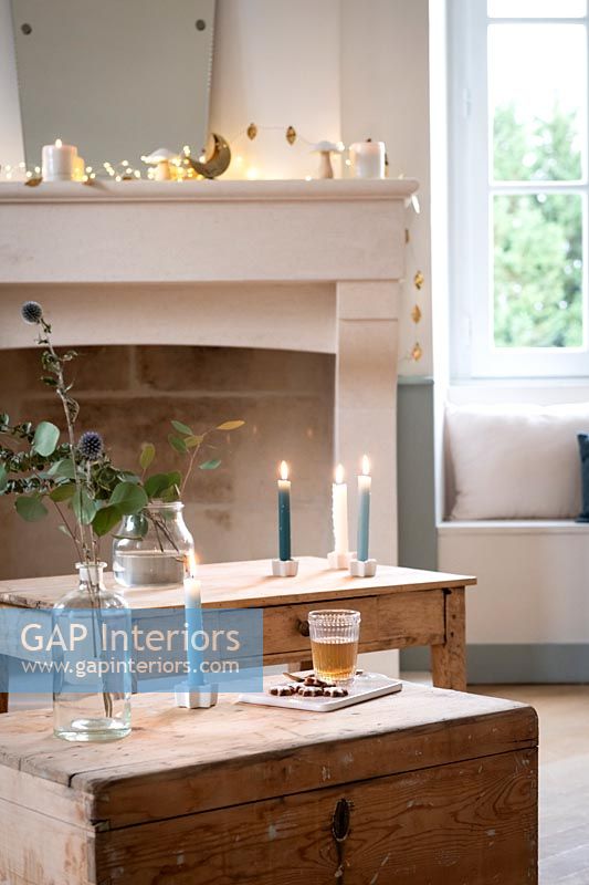 Lit candles on wooden furniture and fairy lights over mantelpiece 