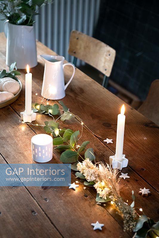 Fairy lights and candles on wooden dining table at Christmas time 
