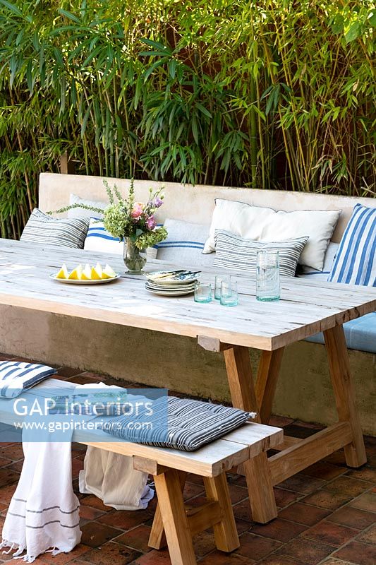 Wooden outdoor dining table with built-in bench seat covered in cushions 