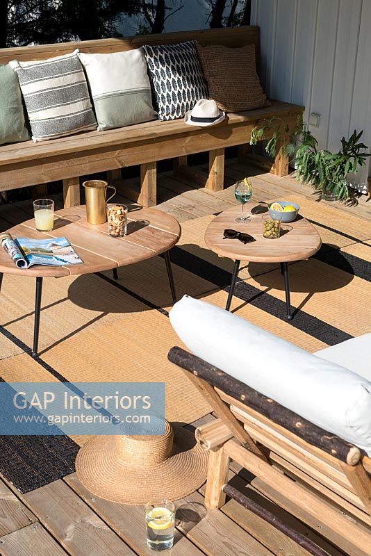 Sunny terrace with wooden furniture, rug and cushions 