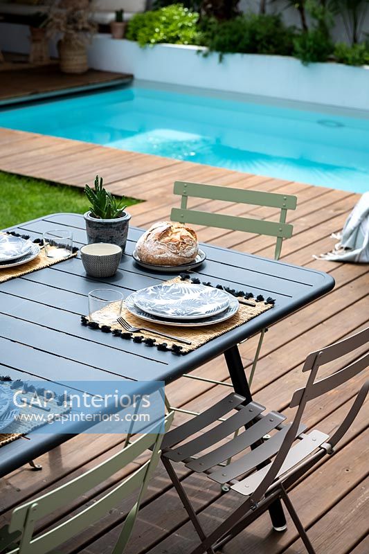 Outdoor dining table laid for lunch next to swimming pool, summer 