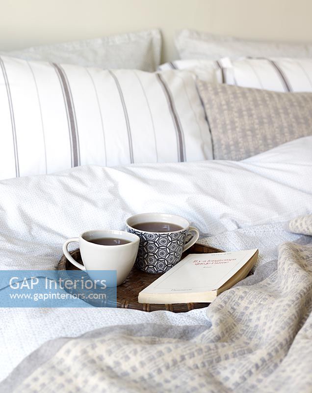 Book and hot drinks on tray in bedroom 