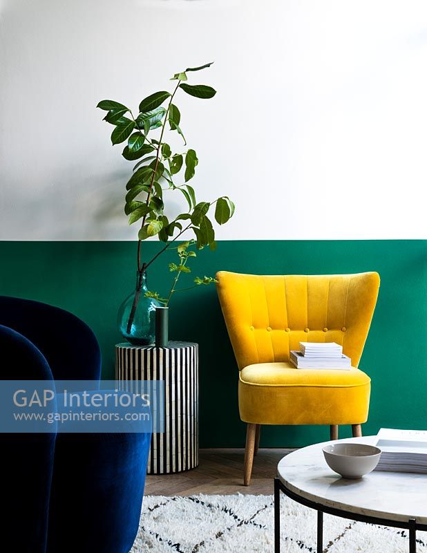 Modern living room with green half painted feature wall behind yellow chair  