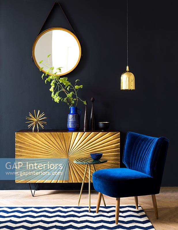 Gold sideboard and blue chair in black painted living room 