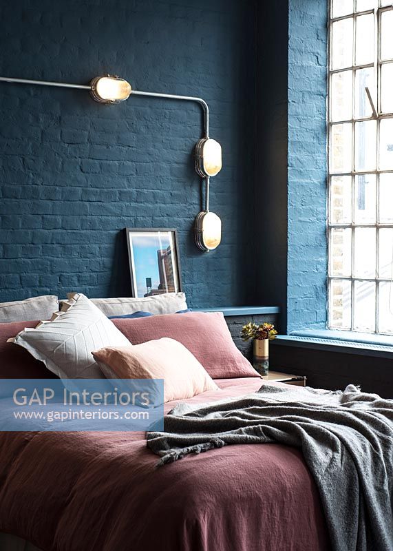 Pink bedding and dark blue painted brickwork in modern bedroom 