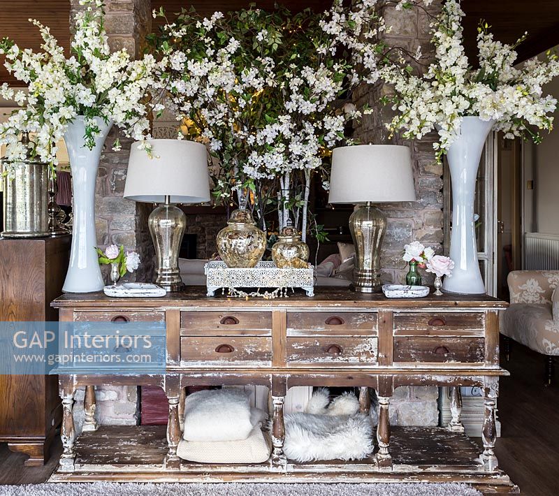 White flowers displayed in large vases on distressed wooden sideboard 