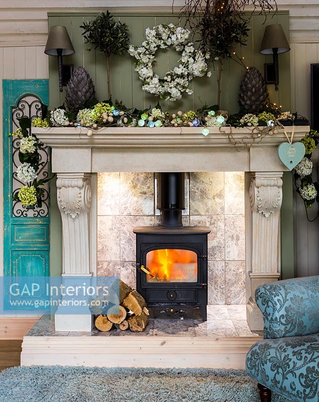 Lit wood burner in large fireplace surrounded by floral decorations 