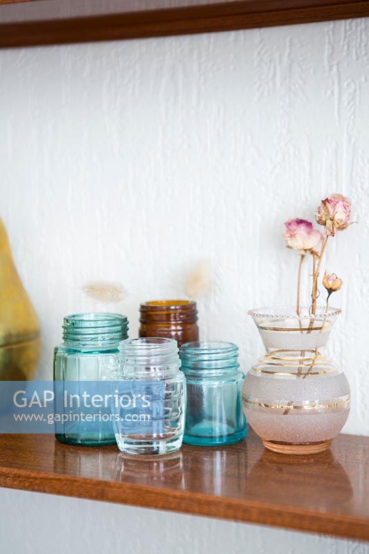 Vase of dried roses and glass jars on wooden shelf  