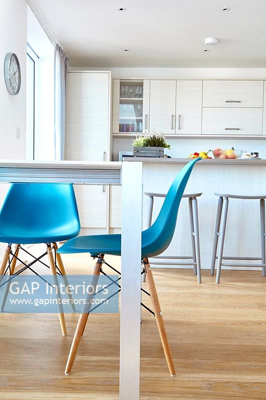 Turquoise chairs in modern white kitchen-diner with wooden floor 
