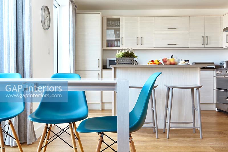 Turquoise chairs in modern white kitchen diner with wooden floor 