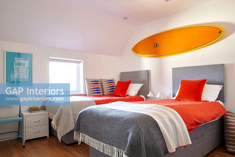 Bright orange surfboard above twin beds 